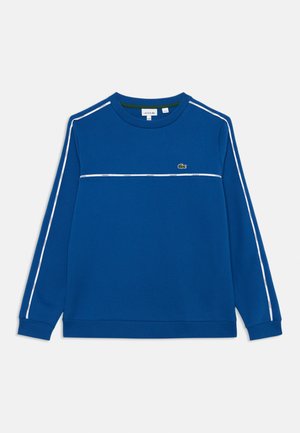 Sweat-shirt bleu à manches longues avec des rayures blanches sur les manches et la poitrine, présentant un petit logo de crocodile vert sur la poitrine gauche.