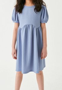 Vaaleansininen mekko, jossa on teksturoitu pinta, lyhyet puffihihat, pyöreä pääntie ja kerrostettu yksityiskohta vyötäröllä. Laskeutuu hienosti helmaan.