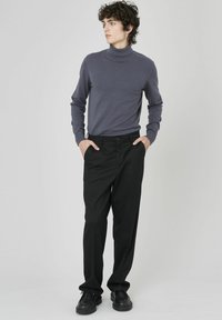 Pull en col roulé gris avec des manches longues associé à un pantalon noir avec un bouton de fermeture, porté avec des chaussures noires. Design minimaliste.