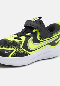 Chaussure de sport noire et jaune néon avec un dessus en maille, une semelle en caoutchouc, un col rembourré et une sangle Velcro. Présente un design de swoosh distinctif.