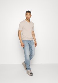 Camiseta de polo de manga corta de color beige con cuello, combinada con jeans de color azul claro y zapatillas deportivas multicolores.