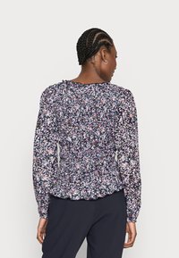 Blusa floral com fundo azul-marinho e padrões multicoloridos, mangas longas, cintura franzida e decote com babados.