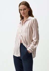 Camicetta bianca con strisce verticali rosse, dotata di colletto e maniche lunghe. La camicia ha una vestibilità comoda e una texture liscia.