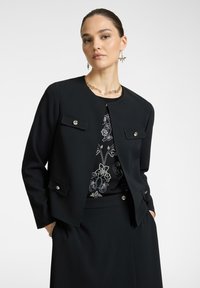 Mustat istuvat takki pyöreällä kauluksella, kahdella etutaskulla ja hopeisilla nappikoristeilla. Pukeutunut kuviollisen yläosan päälle; sileä kangastuntu.