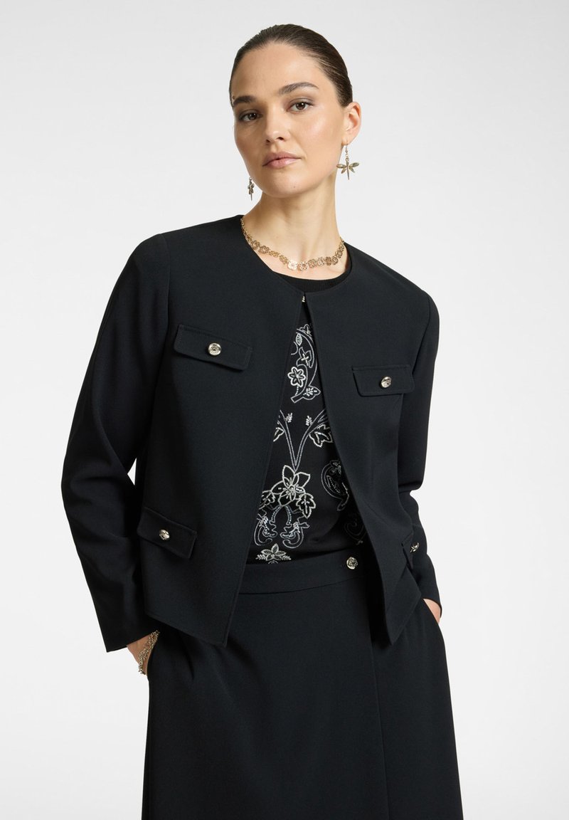 Mustat istuvat takki pyöreällä kauluksella, kahdella etutaskulla ja hopeisilla nappikoristeilla. Pukeutunut kuviollisen yläosan päälle; sileä kangastuntu.