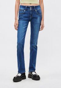 Temno modri džins z ravnim krojem hlačnic, pet žepov in zapiranjem na dva gumba. Ponaša se z rahlim zbledelostjo in kontrastnim šivanjem.