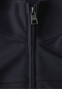 Mörkblå zip-up jacka med hög krage, slätt tyg och en metallisk dragkedja med en stilren dragflik. Synliga sömdetaljer.