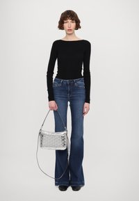 Svart langermet topp, tettsittende; blå slengjeans; sølvfarget metallisk håndveske med teksturert mønster; svarte sko; nøytral bakgrunn.