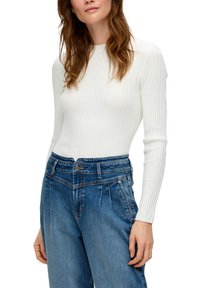 Haut à manches longues blanc à côtes associé à un pantalon en denim bleu taille haute avec un design plissé et une fermeture à boutons à l'avant.