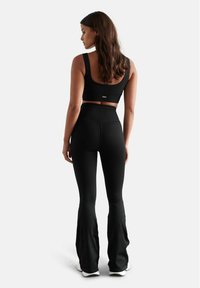 Schwarzes geripptes Crop-Top und hochtaillierte Schlaghosen, die eine glatte Textur und minimale Markenkennzeichnung auf dem Oberteil aufweisen. Figurbetonter Schnitt.