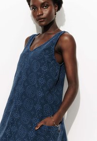 Robe sans manches bleu marine en tissu texturé avec un motif géométrique, dotée d'un décolleté en V et de poches latérales.