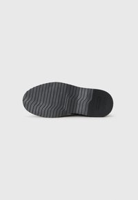 Suela de zapato de goma negra con un patrón de textura en relieve y surcos alternos para mejorar el agarre. Punta redondeada con un borde suave.