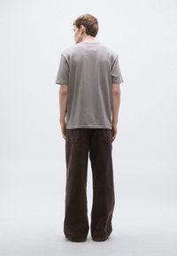 Szürke pamut póló rövid ujjakkal, bő, sötétbarna nadrággal párosítva. A pólón egy kis részlet található a hátán.