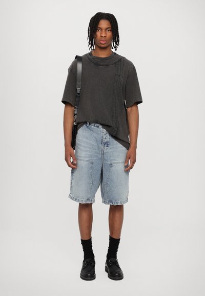 Black oversized t-shirt with textured detailing, light blue denim shorts, black socks, and black shoes. Simplistic, contemporary casual outfit.