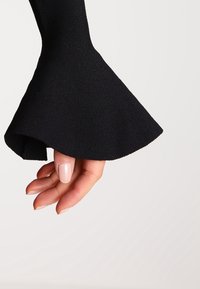 Schwarzer, gerippter Stoff mit einem glockenförmigen Ärmel. Sichtbare Hand mit kurzen, manikürten Nägeln. Glatte Textur, tailliertes Design.