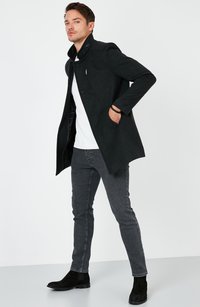 Abrigo de mezcla de lana negra con cuello alto, bolsillo con cremallera y detalles de botones. Combinado con jeans grises y botas de tobillo de ante negras.