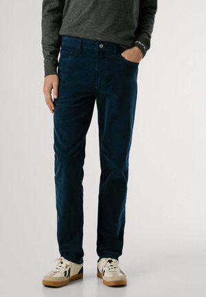Navyblauwe katoenen broek met een gladde textuur, rechte pijpen en voorzakken, gecombineerd met witte sneakers met zwarte accenten.