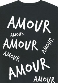 Czarna koszulka z napisem "AMOUR" w różnych stylach, rozmiarach i orientacjach białej czcionki na tkaninie.