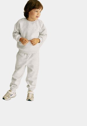 Szara, nakrapiana bluza i dopasowane dresy z elastycznymi mankietami, w zestawie z beżowo-szarymi sneakersami. Prosty, casualowy design.