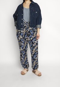 Jeansjakke, lyseblå top, blomsterprintede bukser i marineblå, beige og blå, med bløde lyserøde slip-on sandaler med en sløjfedetalje.