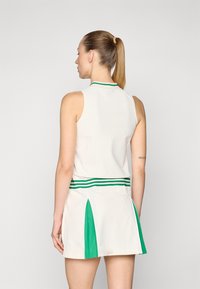 Bezrūpju balta kleita ar zaļu svītrotu apkakli un jostas vietu; iekļautas zaļas sānu paneļi papildu dizaina sīkumiem. Gluda auduma tekstūra.