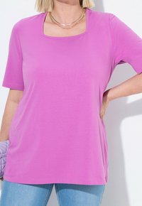 Růžové tričko s krátkým rukávem a čtvercovým výstřihem, vyrobené z měkké látky. Má volnější střih a boční rozparky pro snadný pohyb.