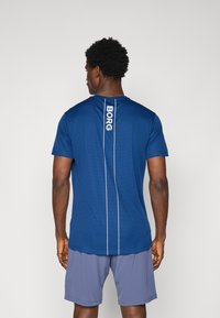 Blauw sportshirt met korte mouwen, voorzien van een wit verticale "BORG" logo en zijnaaddetails. Gecombineerd met grijze shorts.