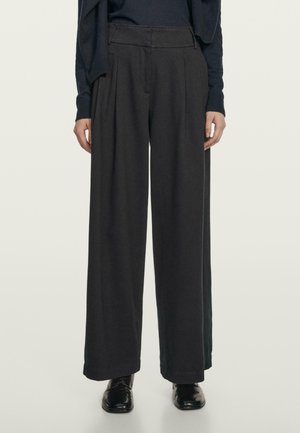 Czarne spodnie o szerokich nogawkach z wysokim stanem, z zakładkami i gładką fakturą, połączone z czarnymi skórzanymi butami.