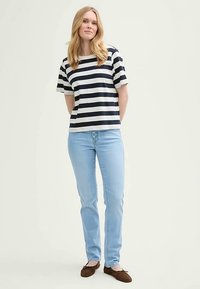 Triibuline lühikeste varrukatega topp tumesinises ja kreemjas toonis, kombineeritud helesiniste teksadega. Modell kannab pruune libiseva sisse jalutatavaid kingi ja seisab neutraalse tausta ees.