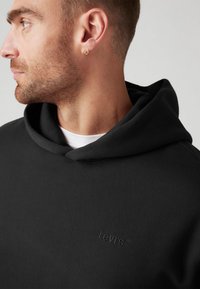 Sudadera negra hecha de una mezcla de algodón con una textura suave. Presenta un bolsillo tipo canguro, capucha con cordón y un logo tonal de Levi's.
