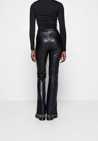 Svarta fusk läderbyxor med utsvängd design och hög midja. Slät textur med en elegant design. Skorna har en mönstrad, färgglad sula.