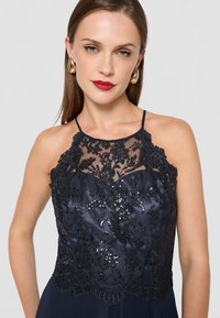 Tengerészkék ruha, bonyolult fekete csipke részletekkel és flitterekkel a áttetsző felső részen. Állítható pántok és sima selyem szoknya.