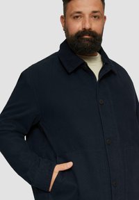 Navy blue button-up coat with a corduroy collar, two front pockets, and a relaxed fit. Made from a textured fabric.