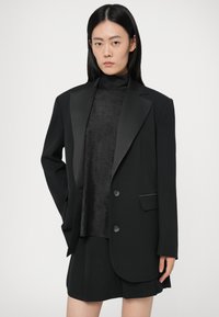 Zwarte op maat gemaakte blazer met satijnen revers en twee knopen, gecombineerd met een zwarte nektop en rok, met een gladde textuur.