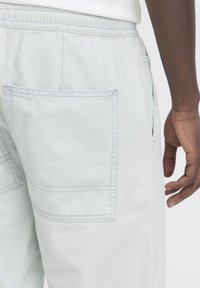 Svetlo sive kratke hlače iz mehkega blaga imajo elastičen pas, stranske in zadnje žepe ter detajle z kontrastnimi šivi.