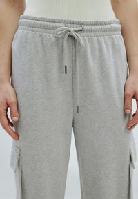 Lichtgrijze sweatpants gemaakt van zacht materiaal, met een elastische tailleband met een trekkoord en cargozakken aan de zijkanten.