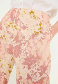 Flowy pink trousers with a floral print in white and green accents, featuring a textured fabric and a wide waistband.