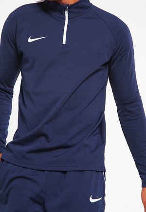 Granatowa, długorękawowa koszulka sportowa z kołnierzem na zamek błyskawiczny. Miękki, elastyczny materiał z białym logo Nike na lewej piersi.