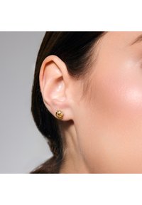 Złote kolczyki wkręty z designem węzła. Gładka tekstura z polerowanym wykończeniem. Mały rozmiar, pewnie przylegają do płatka ucha.