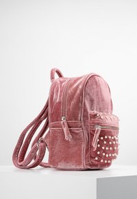 Samtschwarze Rucksack in Rosa mit zwei Reißverschlussfächern, verstellbaren Trägern und dekorativen Perlennieten an der Seitentasche.