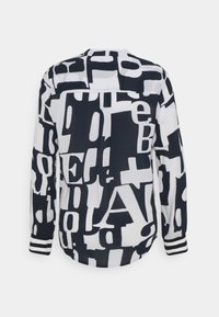 Chemise à manches longues avec motif de grandes lettres abstraites noires et blanches et poignets rayés, vue de dos.