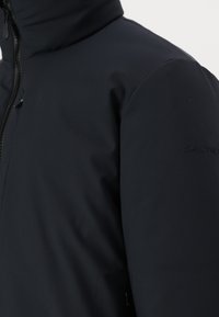 Navy blue waterproof jacket with a high collar, zip closure, and textured fabric. Features a subtle embossed logo on the sleeve.