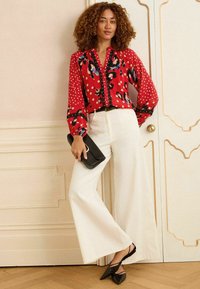 Sarkans blūze ar punktiņiem un ziedu rakstiem, apvienota ar baltām platām biksēm. Melna soma un smaili deguni apavi noslēdz izskatu.