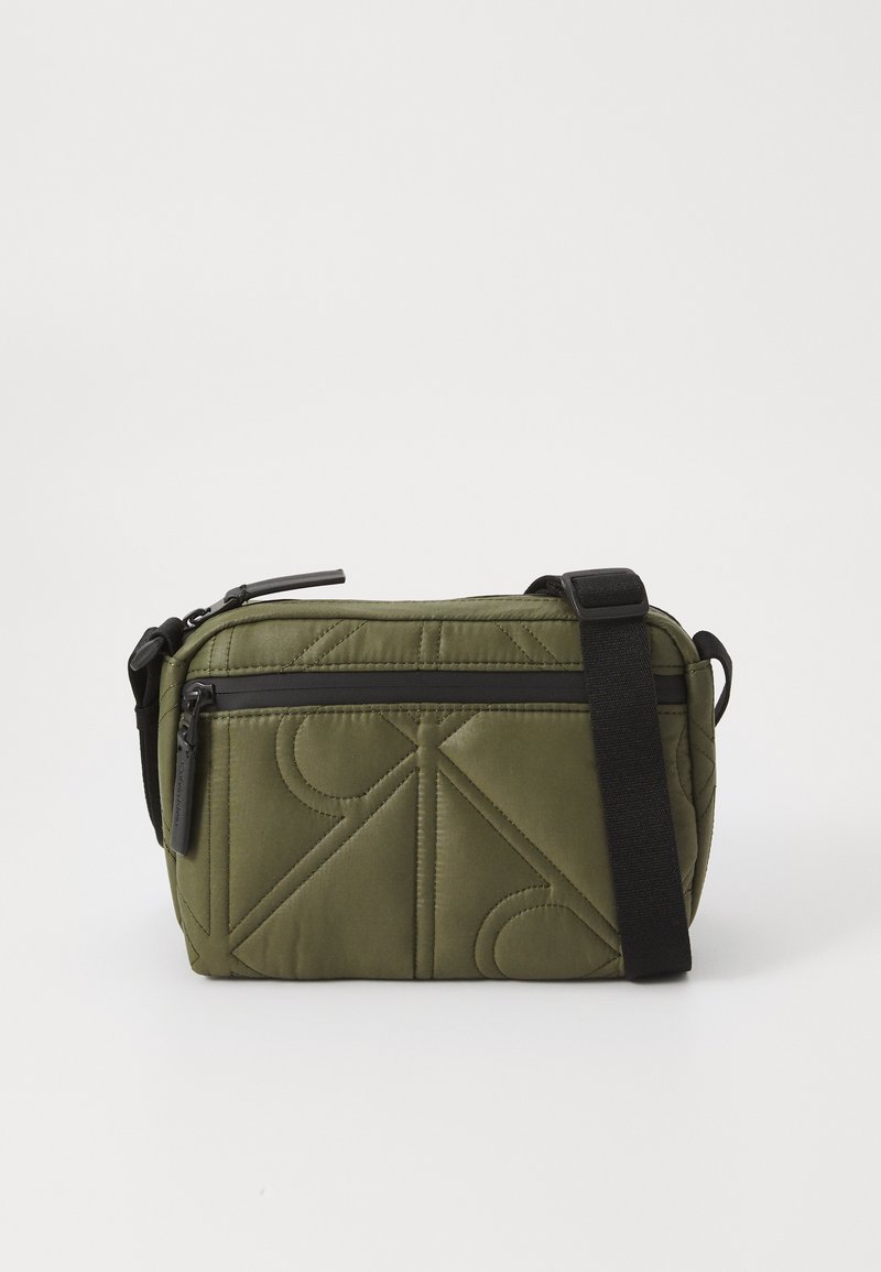 Borsa in tessuto trapuntato verde oliva con una tracolla nera, dotata di chiusura a zip superiore e tasca esterna con zip decorata con motivi geometrici.