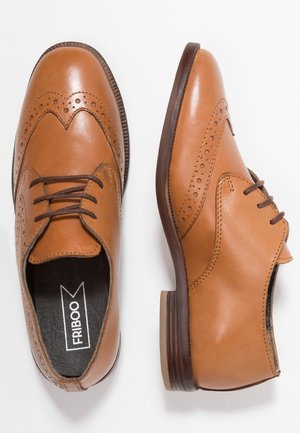 Paire de chaussures habillées brogue en cuir fauve avec perforations décoratives et lacets marron, vues de dessus et de côté.