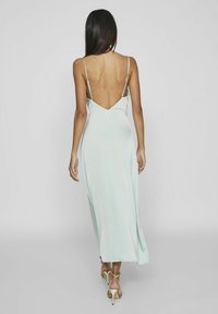 Ljusblå satinmaxiklänning med låg rygg, tunna band och en flödande silhuett. Har en slät yta och elegant fall.