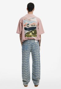 Lyserød oversized T-shirt med et abstrakt bjergmotiv på ryggen. Blå og hvide mønstrede brede bukser med en baglomme.
