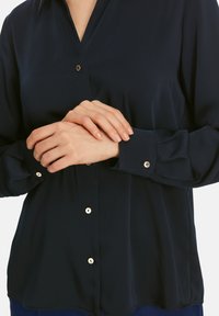 Marineblaues Hemdbluse aus glattem, leichtem Material. Verfügt über goldfarbene Knöpfe, einen klassischen Kragen, lange Ärmel und knöpfbare Manschetten.