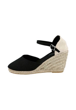 Zapato de cuña negro de punta cerrada con tacón de cuerda tejida, parte trasera beige y correa negra en el tobillo con hebilla plateada sobre fondo blanco.