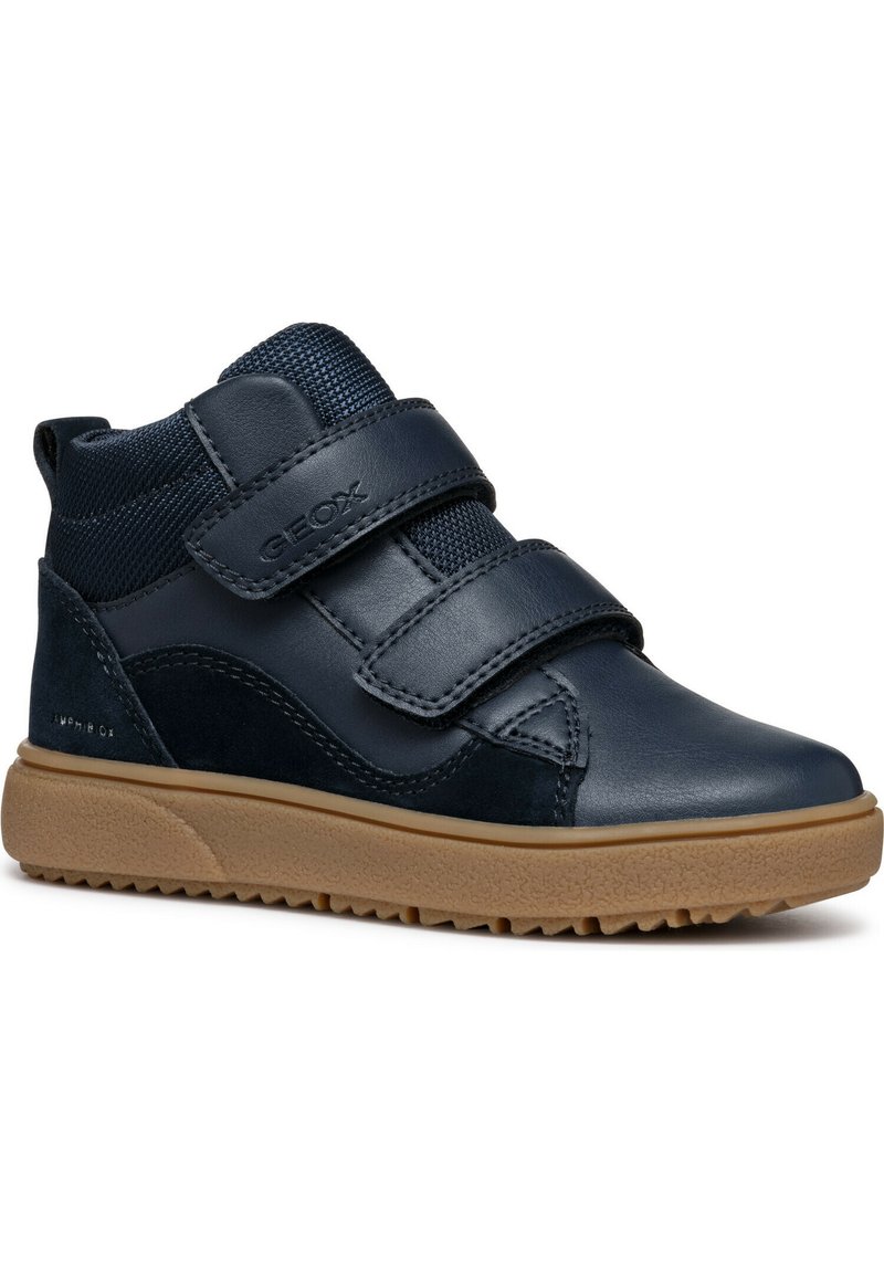 Baskets montantes bleu marine avec double bande velcro, col en tissu texturé, accents en daim et semelle en caoutchouc beige avec motif antidérapant.